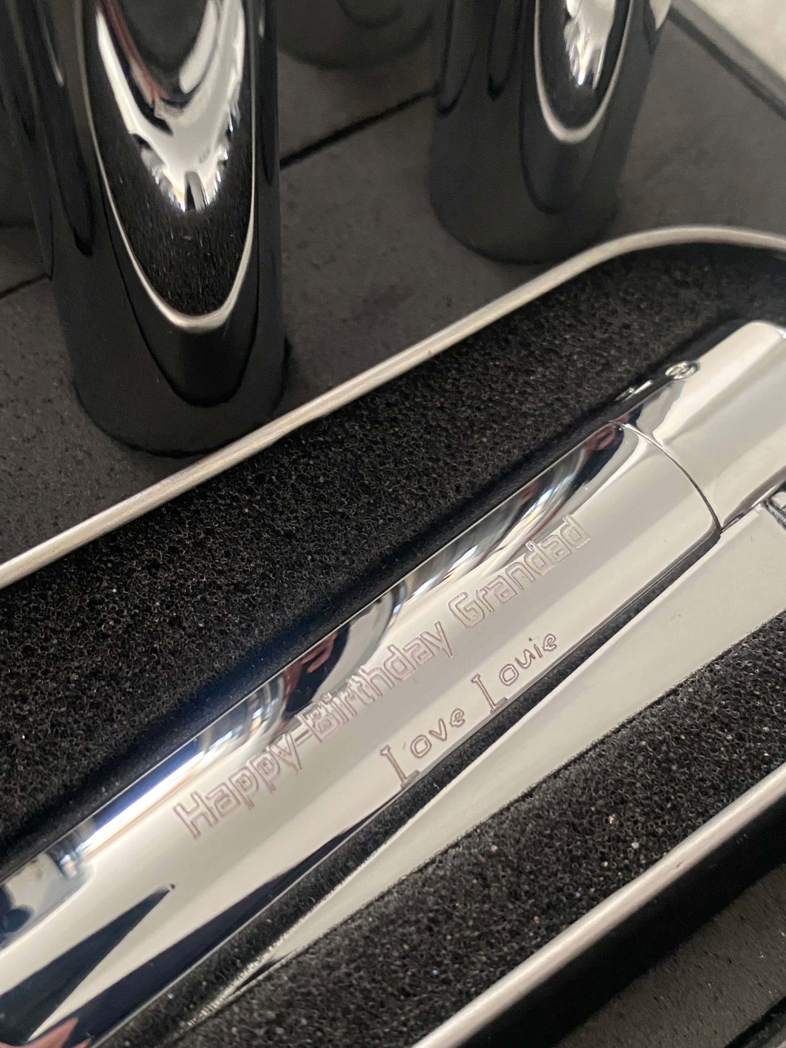 Close up of a chrome clipper lighter  with 'Happy Birthday Grandad' engraved on it.