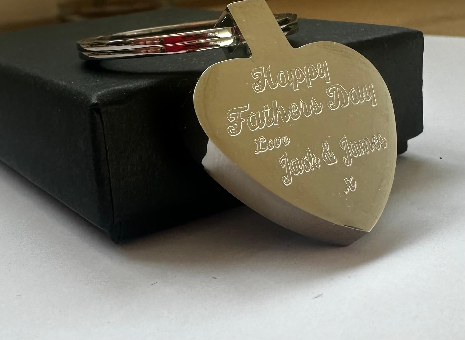 Gold heart-shaped keychain with 'Happy Father's Day' text on a black box